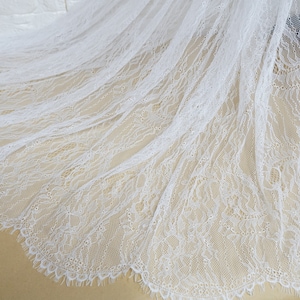May include: White lace fabric with a delicate floral pattern. The lace has a scalloped edge and is soft and sheer.
