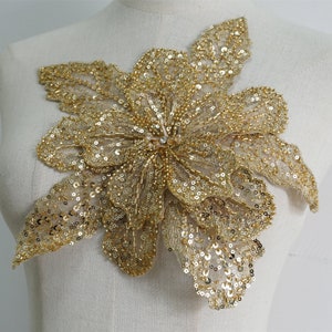 May include: Gold sequined flower applique with a delicate mesh fabric. This embellishment is perfect for adding a touch of sparkle to clothing, accessories, or home decor projects.