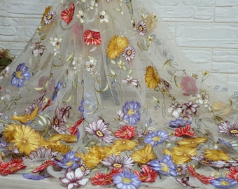 May include: Beige tulle fabric with embroidered floral designs in shades of red, yellow, blue, and white. The flowers are arranged in a random pattern and have a delicate, vintage look.