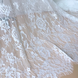 May include: White floral lace fabric with a delicate pattern and scalloped edge.