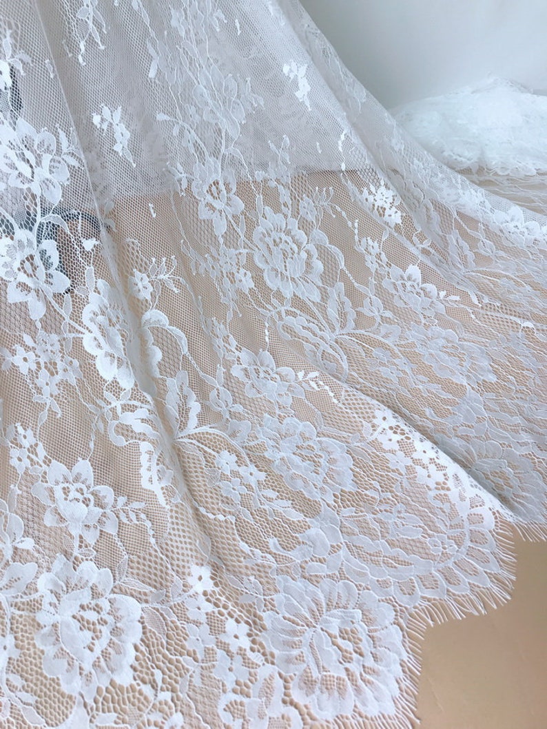 May include: White floral lace fabric with a delicate pattern and scalloped edge.