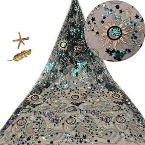 May include: A sheer fabric featuring celestial embroidery with gold suns, moons, and stars accented by teal and silver sequins. The design includes swirling patterns and cloud motifs. A gold starfish and a gold leaf ornament are placed to the left.