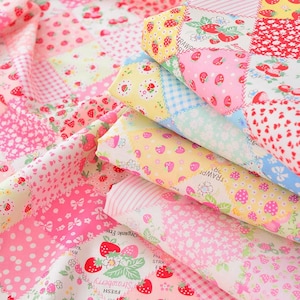 May include: A stack of colorful fabric with a patchwork design. The fabric features various patterns, including strawberries, polka dots, and floral prints in shades of pink, red, yellow, and white. The fabric is folded, showing the different patterns.