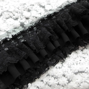 May include: Black lace trim with a ruffled edge, layered over a white fabric with a floral pattern.