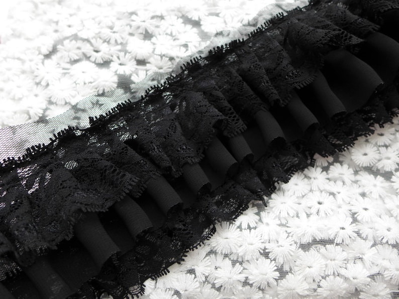 May include: Black lace trim with a ruffled edge, layered over a white fabric with a floral pattern.