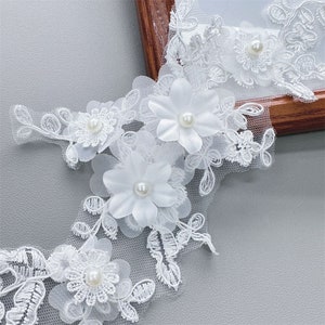 May include: White lace trim with delicate floral appliques and pearl embellishments. The trim features a repeating pattern of flowers and leaves.
