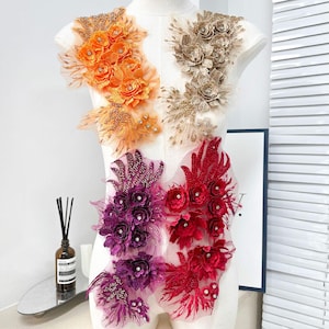 May include: Four distinct floral lace appliques arranged on a mannequin. The top left is orange, top right is gold, bottom left is purple, and bottom right is red. Each piece features layered fabric petals, intricate embroidery, and small clear rhinestones.