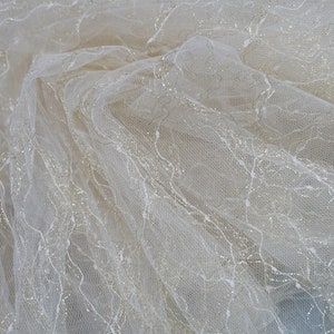 May include: White tulle fabric with a delicate silver glitter pattern. The fabric is soft and sheer, with a subtle shimmer.