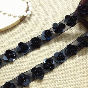 Puede incluir: Borde negro de lentejuelas con un diseño floral sobre una cinta negra transparente. El borde es perfecto para añadir un toque de brillo a cualquier proyecto.