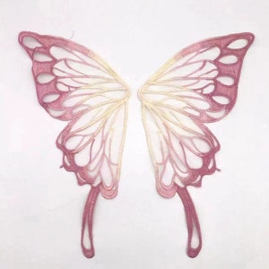 May include: A pair of delicate, pink and white butterfly wings with a lace-like design. The wings are made of a sheer fabric and have a gradient effect, fading from pink to white.