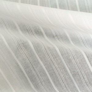 May include: White cotton fabric with thin, vertical stripes. The fabric has a slightly textured surface.
