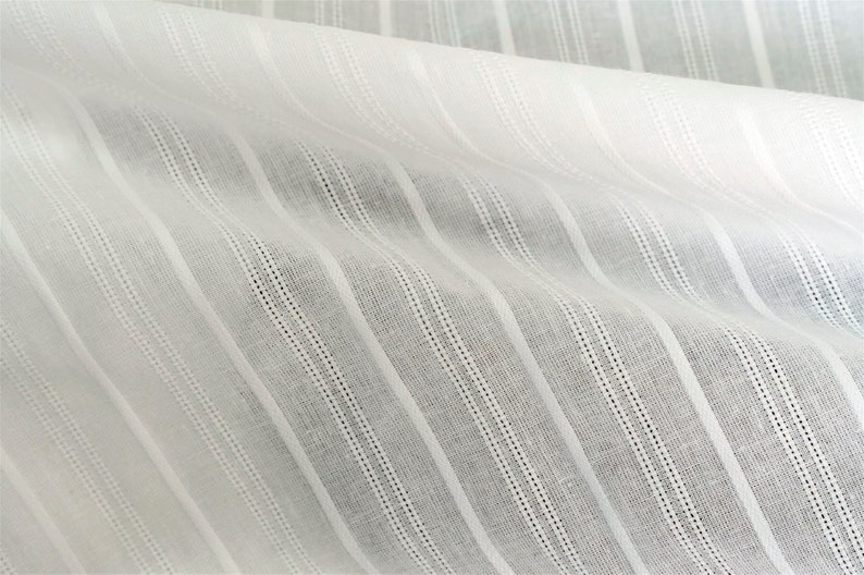May include: White cotton fabric with thin, vertical stripes. The fabric has a slightly textured surface.