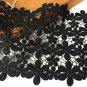 May include: Black lace trim featuring a floral design. The lace is delicate and intricate, with small flowers and a fine mesh pattern.
