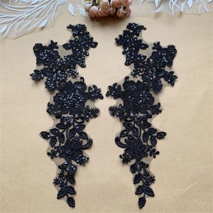 Könnte beinhalten: Zwei schwarze florale Spitzenapplikationen mit Paillettenakzenten. Die Applikationen weisen aufwendige Blumen- und Blattmuster auf, ideal zum Verzieren von Kleidungsstücken oder Accessoires. Die Spitze ist auf einem transparenten Hintergrund angebracht.