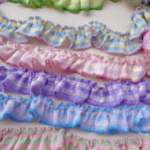 Peut inclure: Gros plan de plusieurs rangées de garnitures en tissu à volants de différentes couleurs pastel. Les garnitures présentent des motifs vichy en bleu, rose, violet et vert, avec des bords festonnés. Idéal pour les projets de couture et d'artisanat.