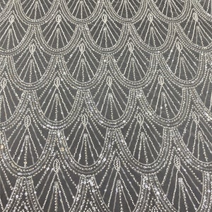 Puede incluir: Tela blanca con cuentas con un patrón geométrico de arcos superpuestos. La tela tiene un brillo sutil y es perfecta para proyectos de artesanía o costura.