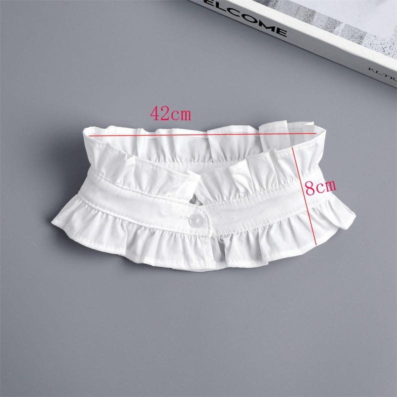 May include: A white, ruffled collar, 42 cm wide and 8 cm high, with a single button closure. The collar is made of a soft fabric and features a layered, frilled design, suitable for adding a vintage touch to any outfit.