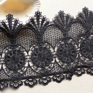 May include: Black lace trim with a delicate floral pattern. The trim features a scalloped edge and a repeating design of small flowers and intricate details.