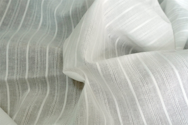 May include: White cotton fabric with thin, vertical stripes. The fabric is woven with a subtle texture and has a soft, drapey feel.