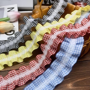 May include: Assortment of ruffled gingham ribbons in black and white, yellow, red, and blue, each with a white lace trim. The ribbons are arranged in a woven basket, showcasing their vibrant colors and textures.