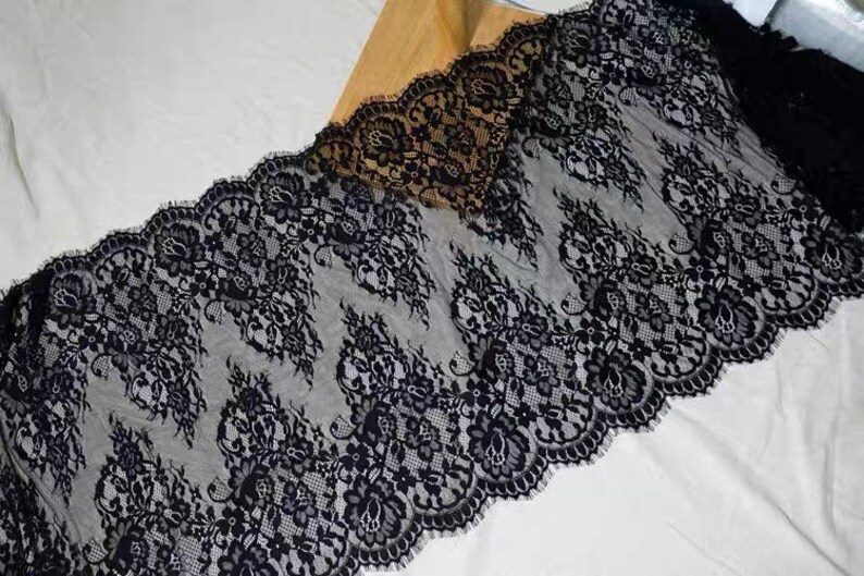 May include: Black lace trim with a delicate floral pattern. The lace is soft and sheer, with a scalloped edge.