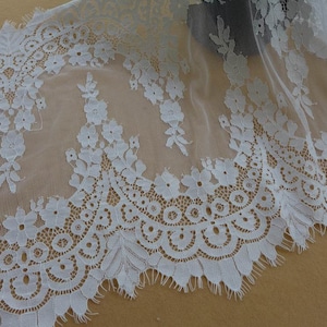 Puede incluir: Borde de encaje blanco con un delicado patr&oacute;n floral y un borde festoneado. El encaje es transparente y tiene una textura suave y fluida.