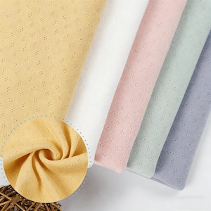 May include: Five folded pieces of fabric in yellow, white, pink, light green, and light blue. Each piece features a repeating small eyelet pattern of tiny four-point stars or crosses. A circular inset shows a close-up of the yellow fabric texture.