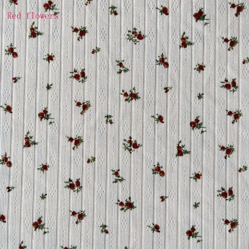 May include: Cream-colored fabric with a vertical ribbed texture and a pattern of small red flowers and green leaves. The text "Red flowers" is in the upper left corner. The floral design is evenly distributed across the fabric.