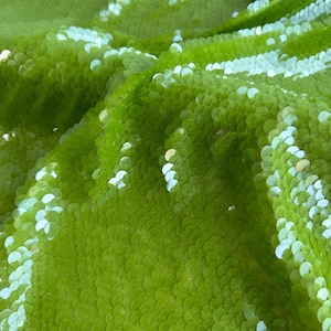 Op de afbeelding: Groene paillettenstof met een glinsterende, iriserende afwerking. De pailletten zijn in een golfpatroon gerangschikt.