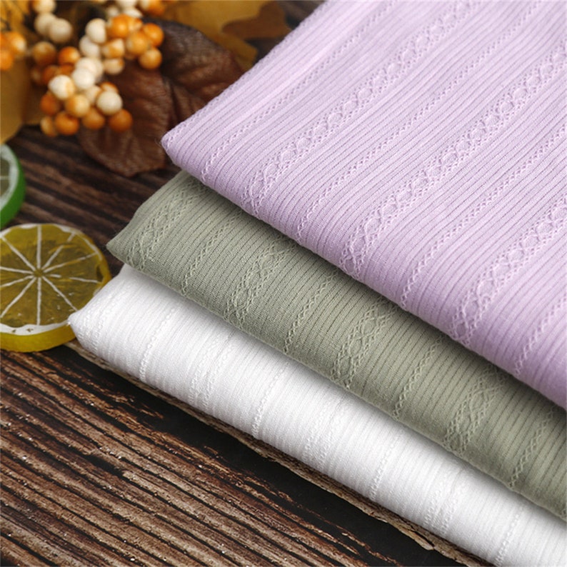May include: Three pieces of fabric in different colors: light purple, light green, and white. The fabric has a ribbed texture and a delicate pattern of small circles.