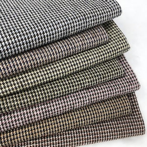 Puede incluir: Una pila de tela de pata de gallo en varios colores, incluyendo blanco y negro, marrón y rosa. La tela tiene un patrón tejido clásico, adecuado para proyectos de ropa y decoración del hogar.