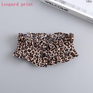 May include: A leopard print accessory with a ruffled edge and a single black button closure. The fabric features a pattern of brown and black spots on a beige background. The text "leopard print" is visible in the image.