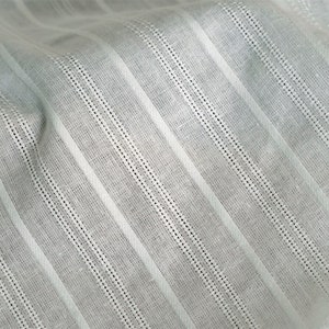 May include: White fabric with thin, vertical stripes. The fabric has a subtle texture and a slightly wrinkled appearance.