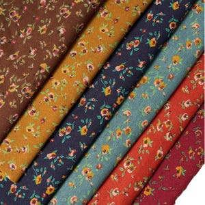 Puede incluir: Muestras de tela en varios colores, cada una adornada con un delicado estampado floral. Las telas van desde el marrón y el amarillo mostaza hasta el azul marino, el verde azulado, el rojo y el burdeos, todas con pequeños diseños florales repetidos.
