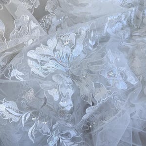 May include: White tulle fabric with a floral pattern embroidered with sequins.
