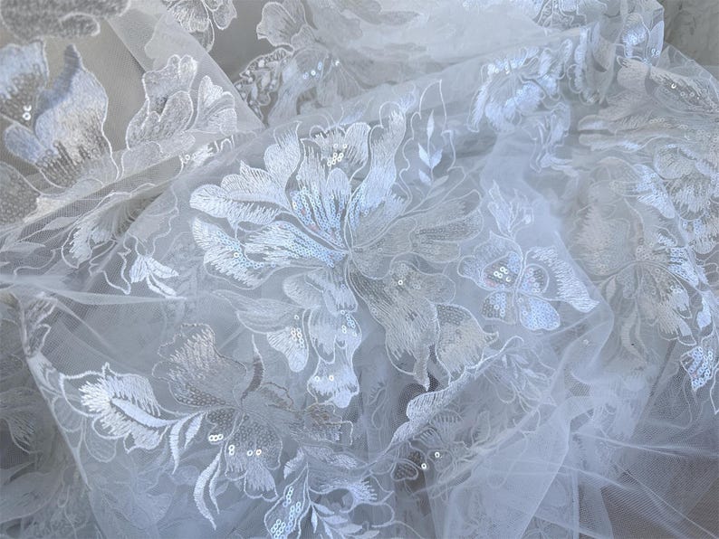 May include: White tulle fabric with a floral pattern embroidered with sequins.