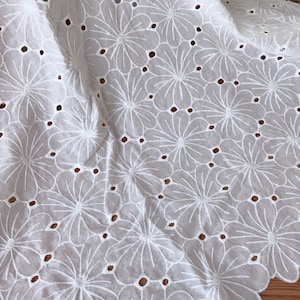 May include: White cotton fabric with a delicate eyelet pattern of small flowers. The fabric has a scalloped edge.