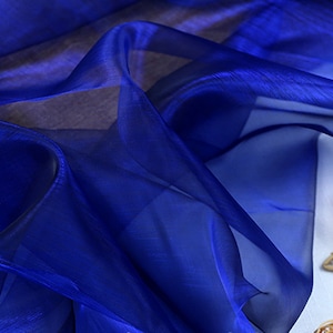 May include: A close-up of a royal blue sheer fabric with a soft, flowing texture. The fabric is draped over a white surface and has a subtle shimmer.