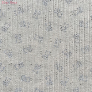 May include: Light gray fabric with a repeating pattern of blue teddy bears. The fabric has a textured, ribbed appearance with small, evenly spaced perforations. The words "Blue Bear" are in the upper left corner.