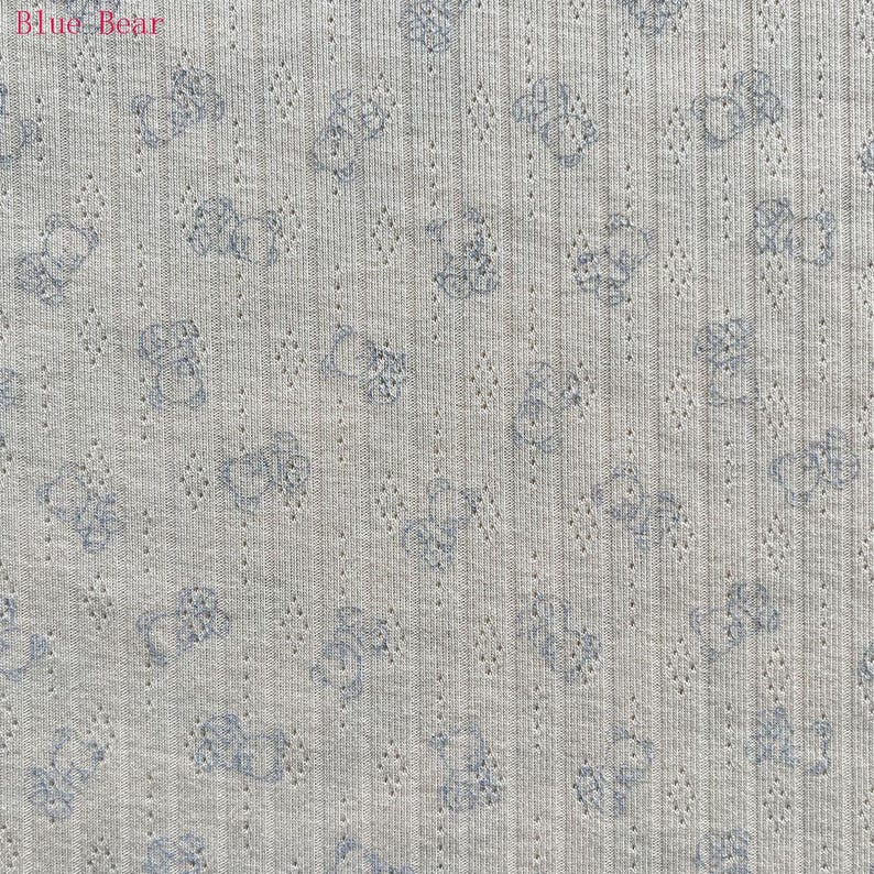 May include: Light gray fabric with a repeating pattern of blue teddy bears. The fabric has a textured, ribbed appearance with small, evenly spaced perforations. The words "Blue Bear" are in the upper left corner.