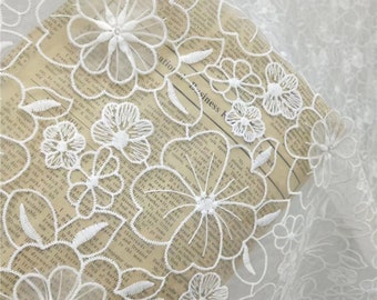 May include: White floral lace fabric with a delicate pattern of flowers. The lace is sheer and has a soft, flowing texture.