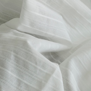 May include: White cotton fabric with a striped texture. The fabric is soft and lightweight, making it ideal for a variety of sewing projects.