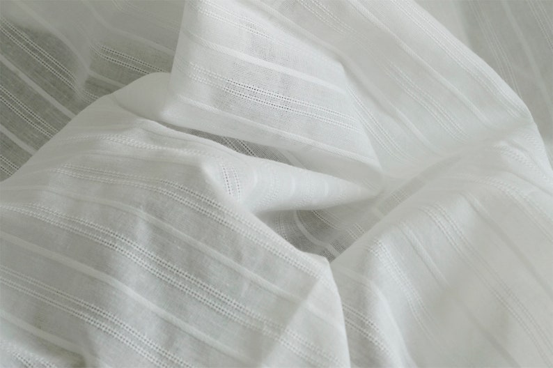 May include: White cotton fabric with a striped texture. The fabric is soft and lightweight, making it ideal for a variety of sewing projects.