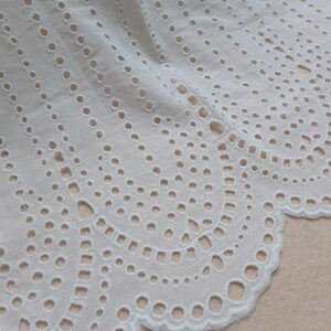 May include: White cotton lace trim with a scalloped edge and a delicate eyelet pattern. The lace has a repeating design of small circles and ovals.