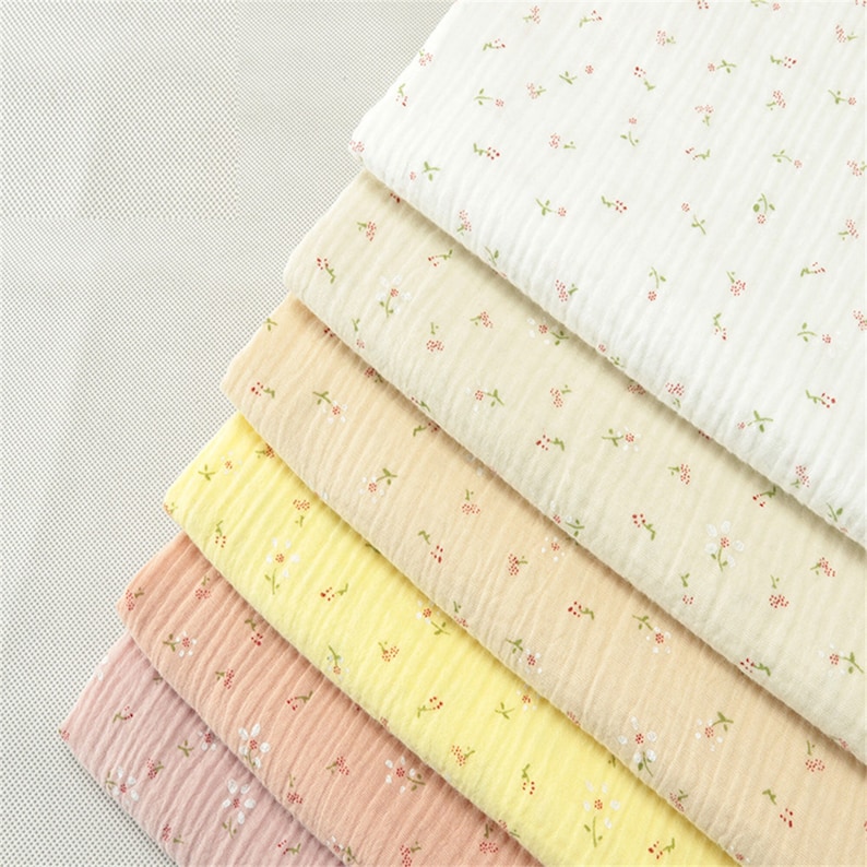 May include: A stack of six fabric swatches in various shades of yellow, pink, and white. Each swatch features a delicate floral print with small white flowers and green stems.
