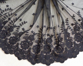 May include: Black lace fabric with a delicate floral pattern. The lace has a scalloped edge and is perfect for adding a touch of elegance to any project.