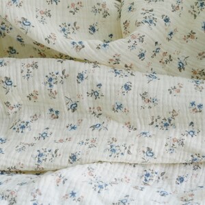 May include: A close-up of a white fabric with a small floral pattern in shades of blue and pink.
