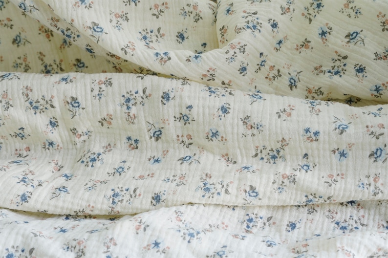 May include: A close-up of a white fabric with a small floral pattern in shades of blue and pink.