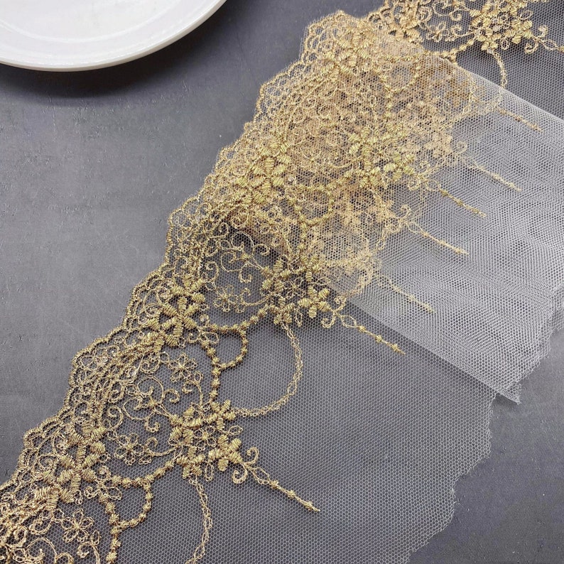May include: Gold lace trim with a delicate floral pattern on a sheer white mesh fabric.