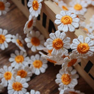 Puede incluir: Borde de encaje blanco en forma de margarita con centros amarillos. El borde está dispuesto en una línea continua, creando un patrón delicado y floral.